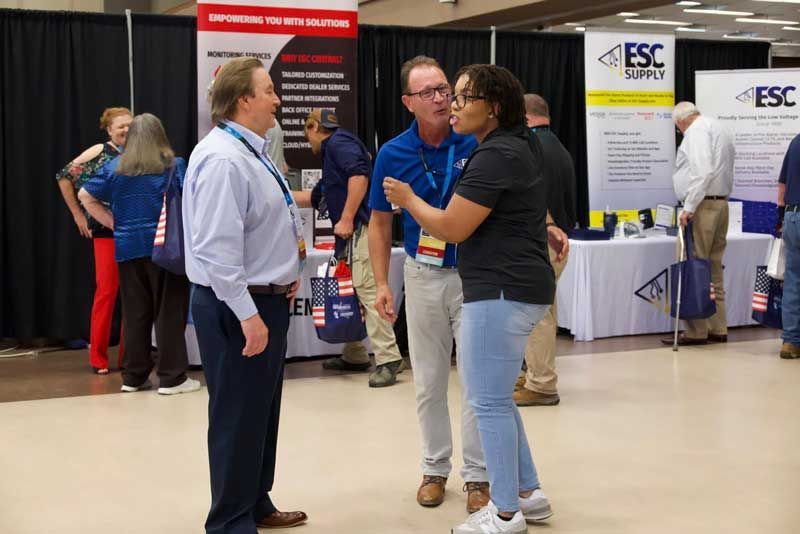 People talking at a trade show with vendor booths in the background.