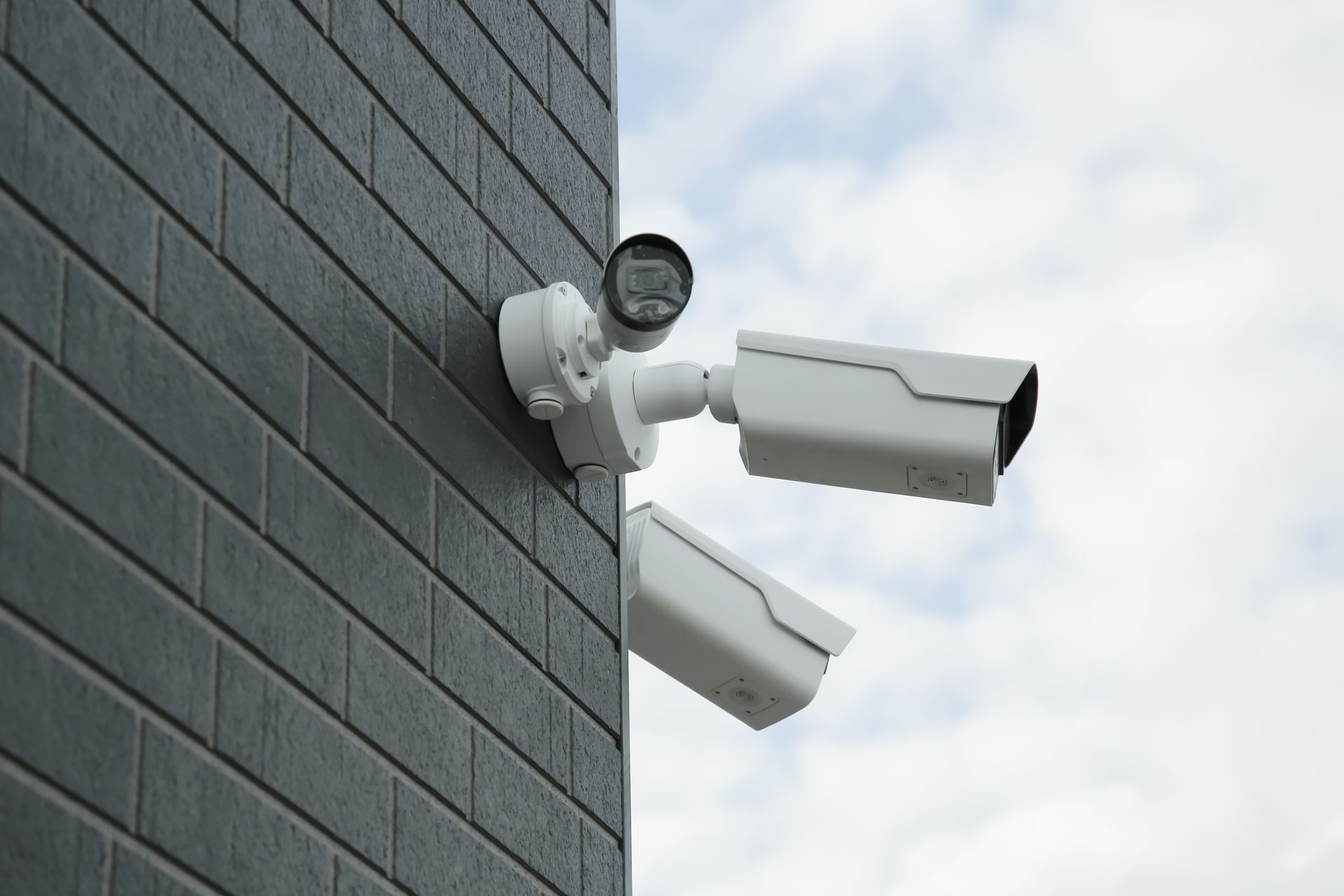 Three white security cameras mounted on a gray brick building.
