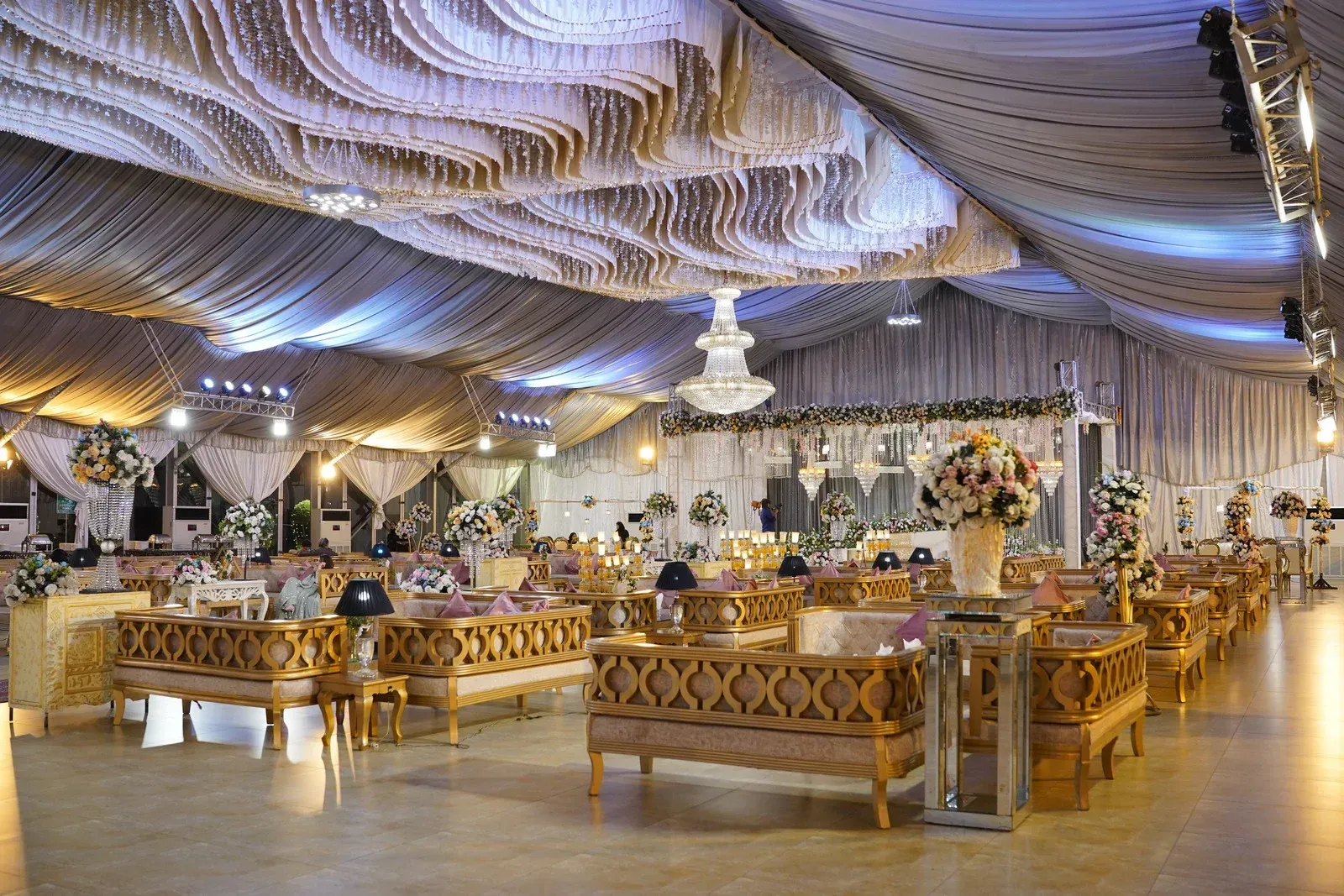 Elegant banquet hall with gold sofas, floral centerpieces, and draped ceiling lighting.