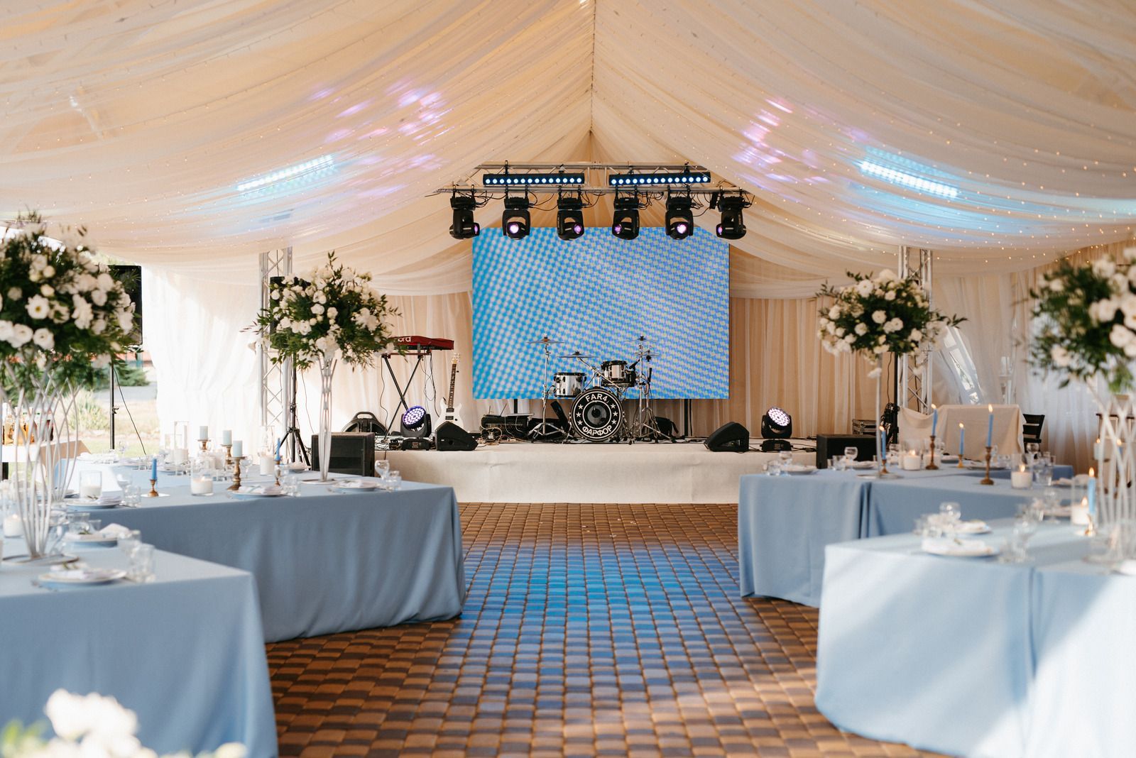 Elegant wedding reception tent with white draping, round tables, and a lit stage at the back