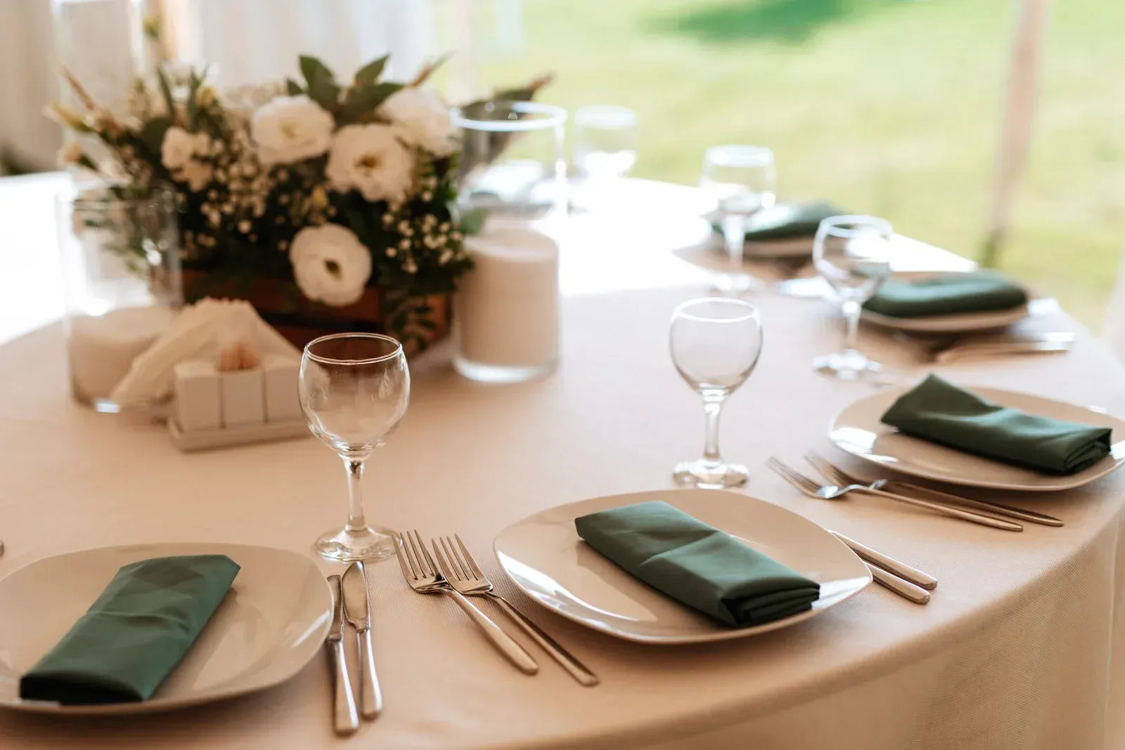 Elegant wedding reception table set with white linens, green napkins, and floral centerpiece outdoors