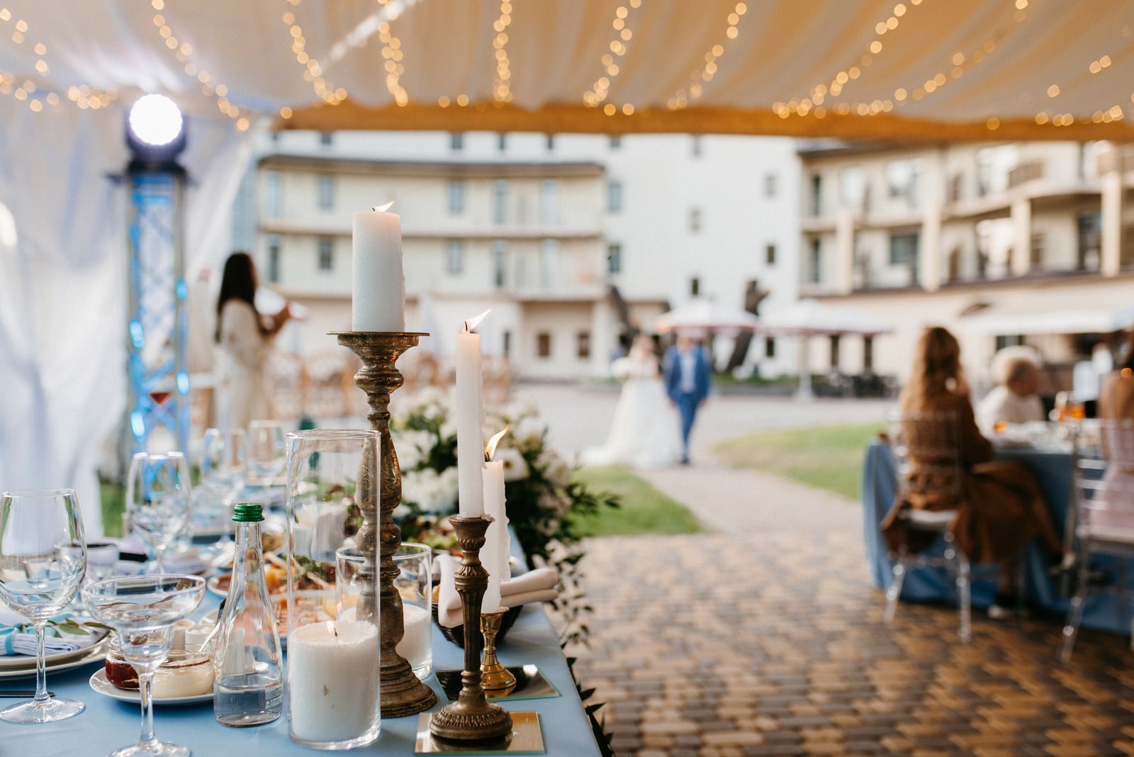 Elegant outdoor banquet table under a tent, with candles and string lights in a courtyard venue