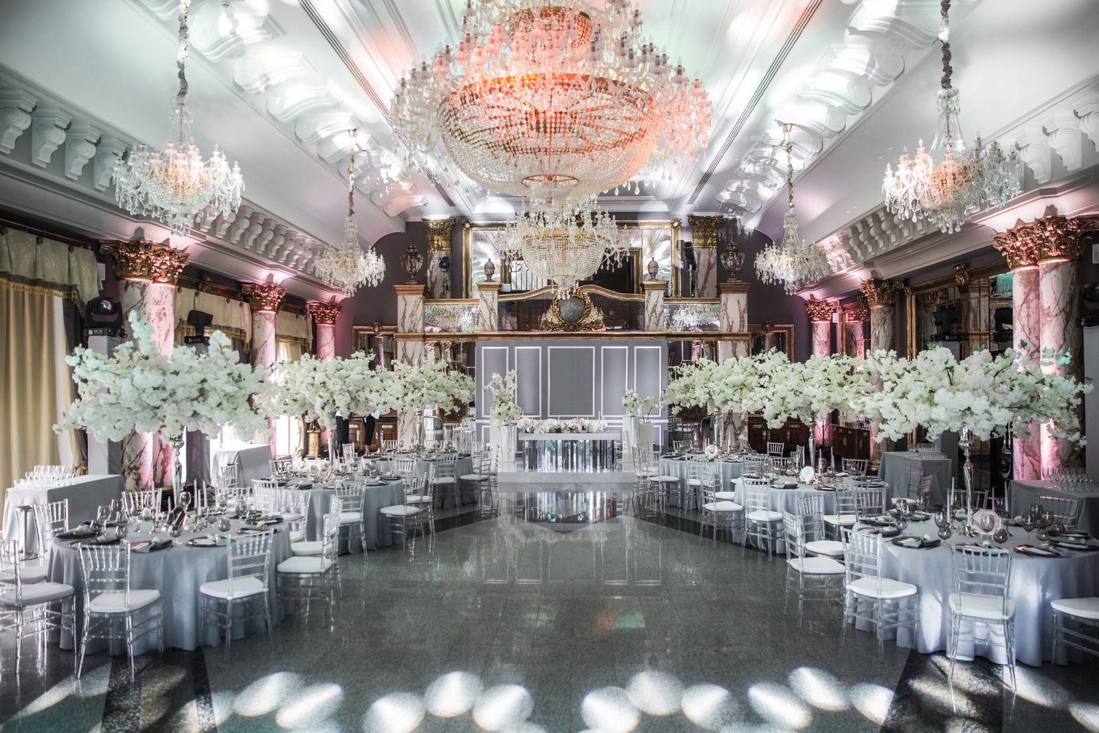 Elegant banquet hall with white floral arrangements, chandeliers, and rows of tables set for a formal event