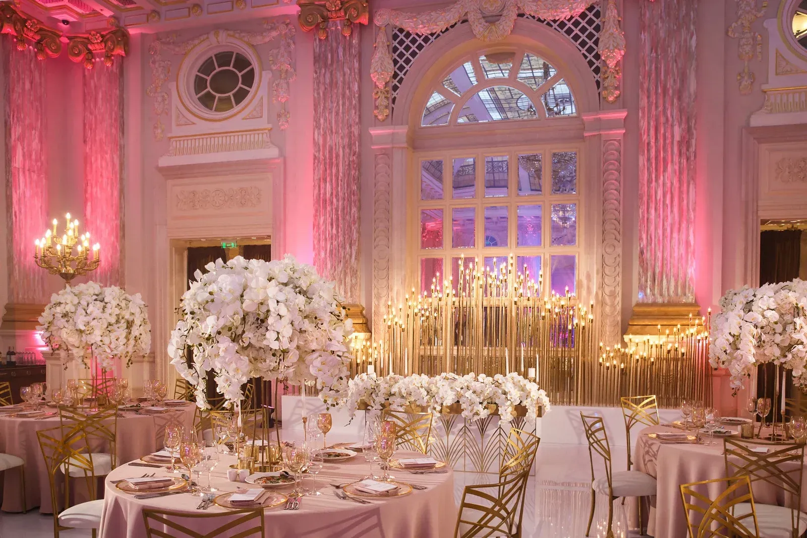 Elegant wedding reception hall with white floral arrangements and pink lighting