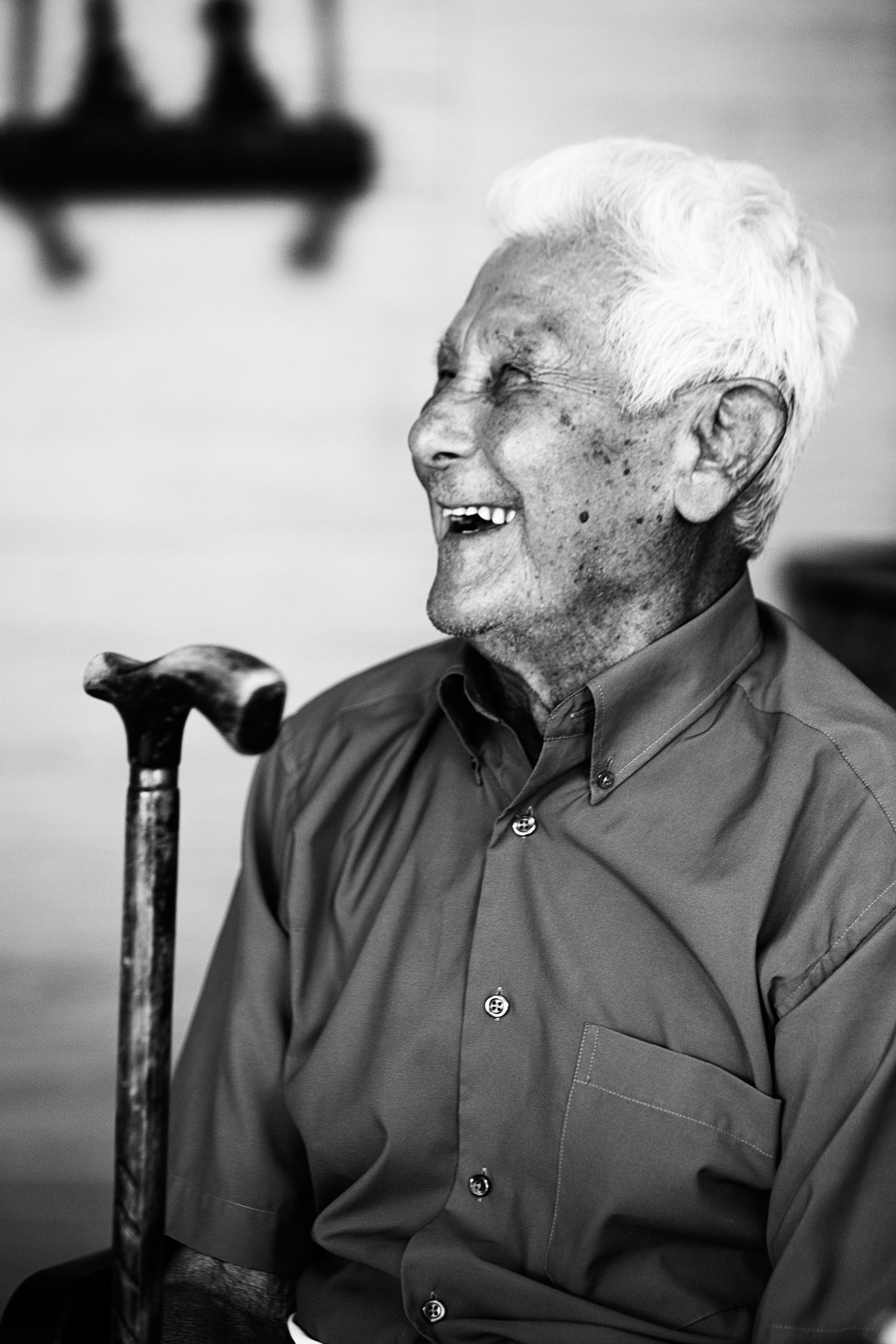 A person with white hair smiling toward the side, holding a walking cane in a black-and-white portrait.