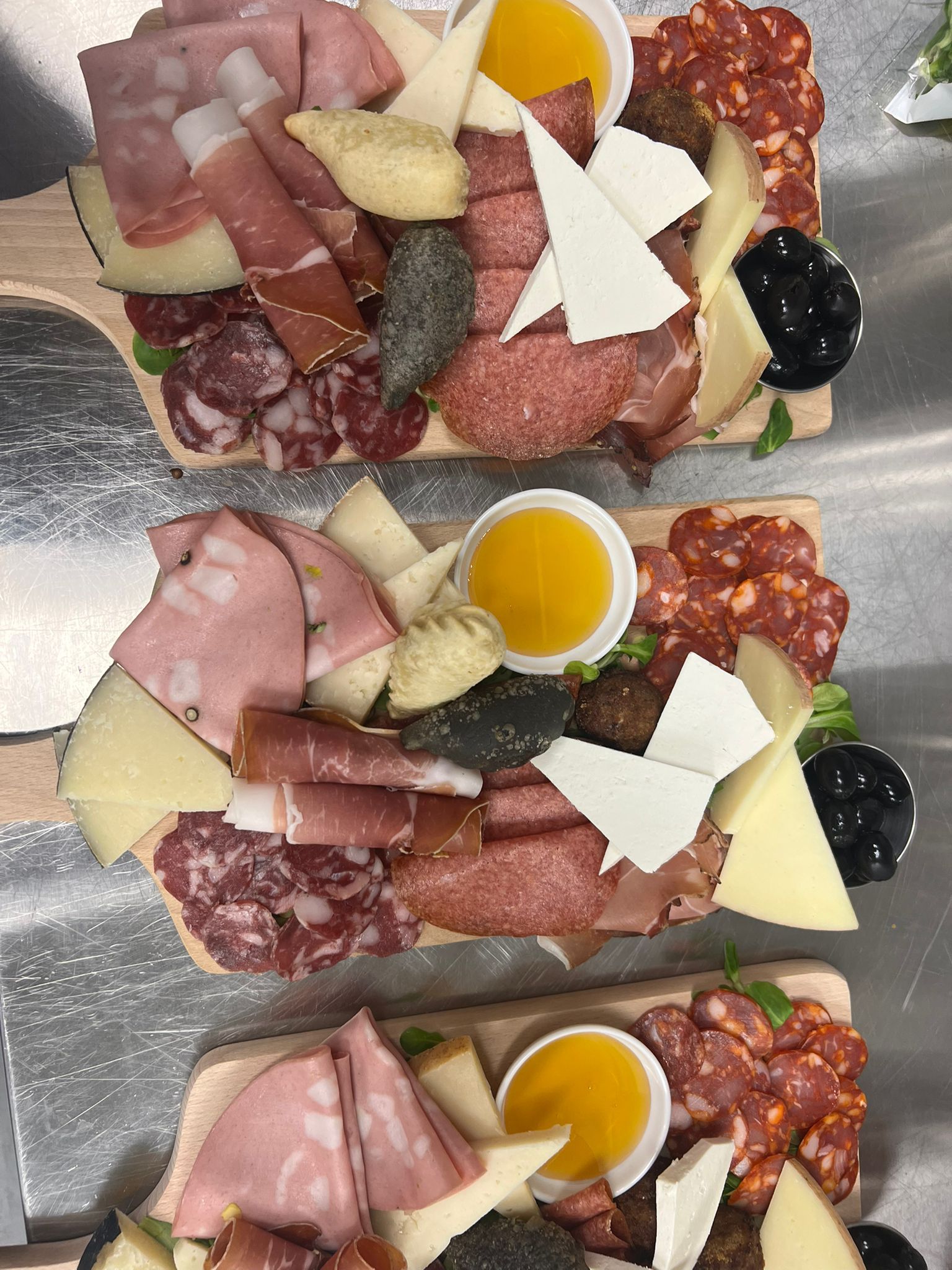 Tre coppette di salumi con salumi, formaggi, cracker, olive e salsa gialla su un vassoio di metallo.