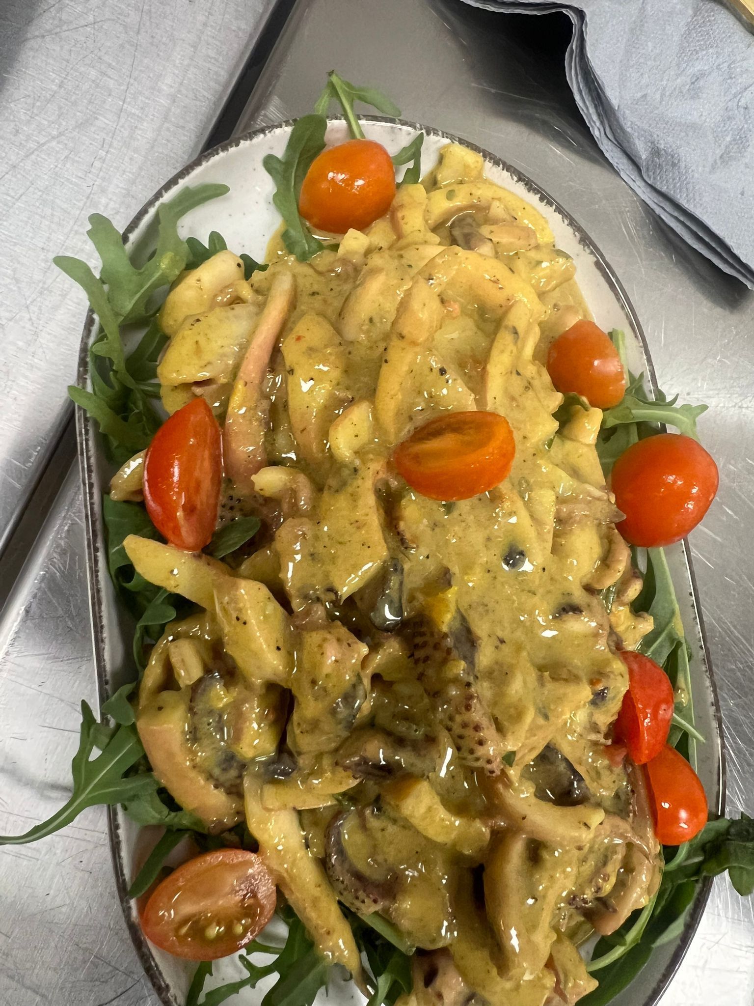 Pasta in salsa cremosa con pomodorini e rucola, servita su un piatto ovale.