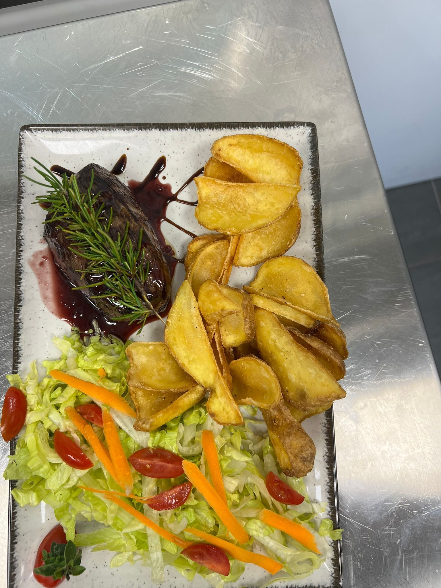 Insalata servita su un piatto con verdure a foglia verde, pomodorini, spicchi di patate fritte e una salsa scura come guarnizione.