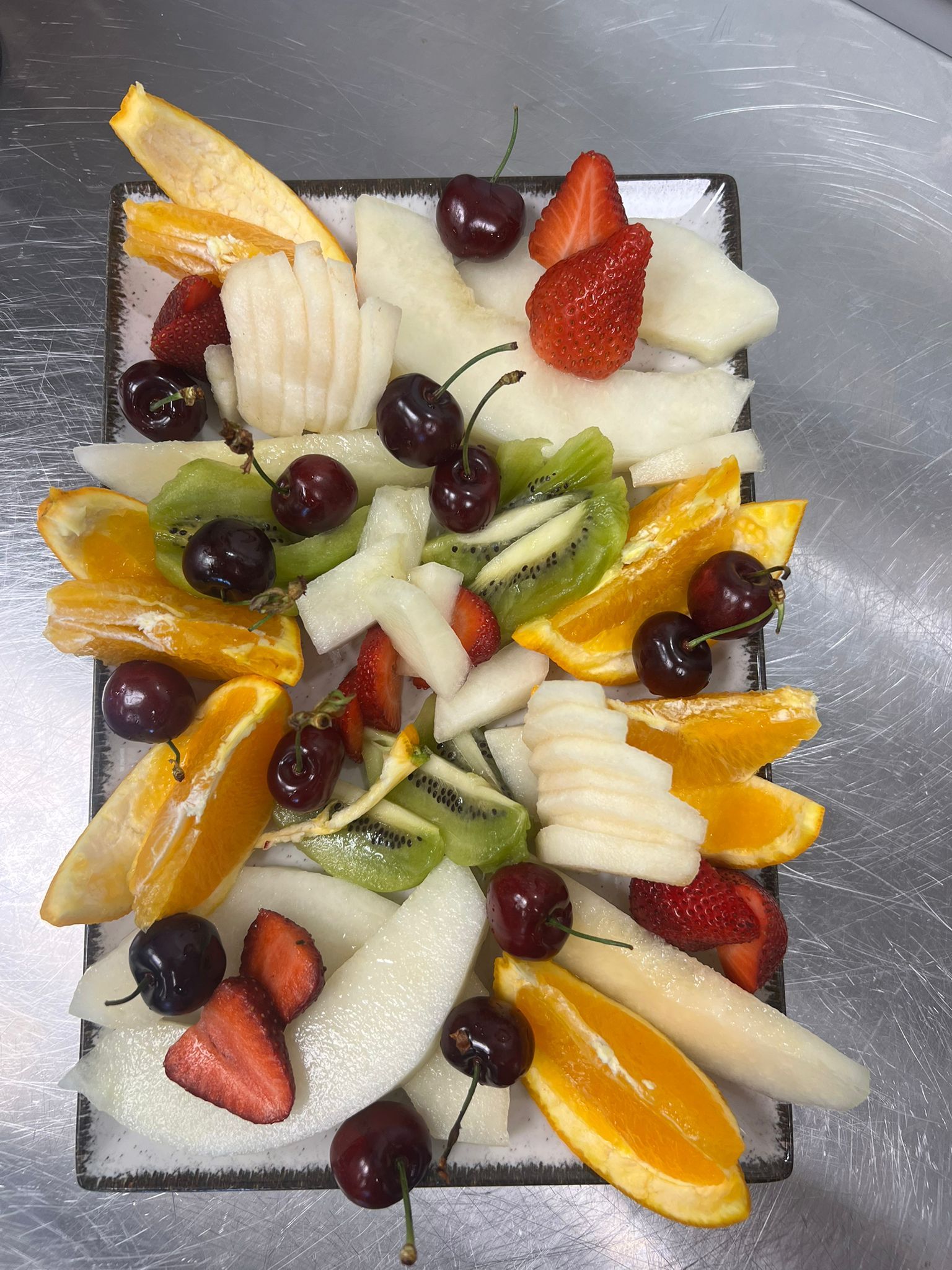 Fette di frutta assortite e frutti di bosco disposti su un piatto rettangolare, colorati e freschi