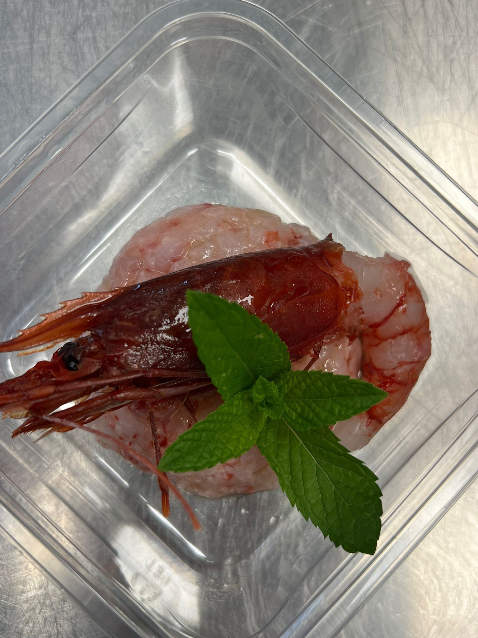 Gamberi cotti con foglie di menta su un piatto quadrato trasparente.