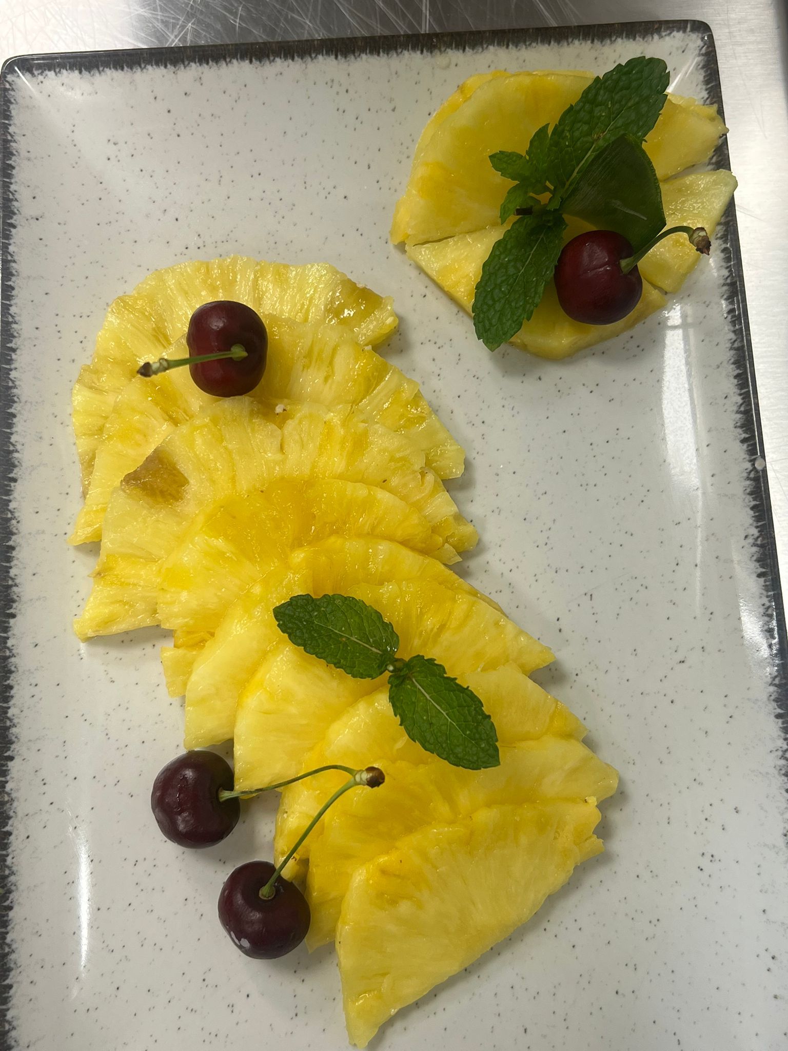 Fette di ananas giallo su un piatto di vetro, guarnite con menta e uva rossa.