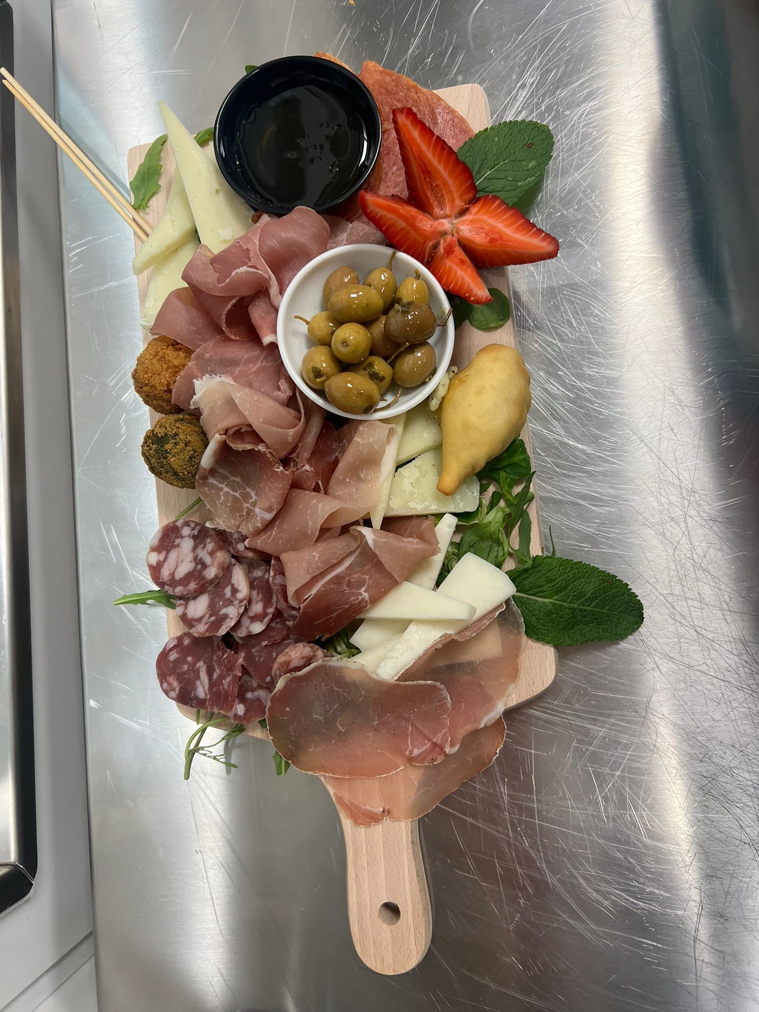 Tagliere di salumi su una paletta di legno con carni, formaggi, olive, fichi, uva e cracker.