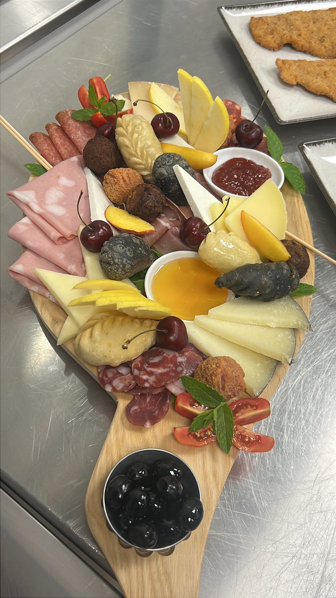 Tagliere di salumi e formaggi con frutta e affettati disposti su un piatto, accompagnato da una ciotolina di marmellata e pane tostato.