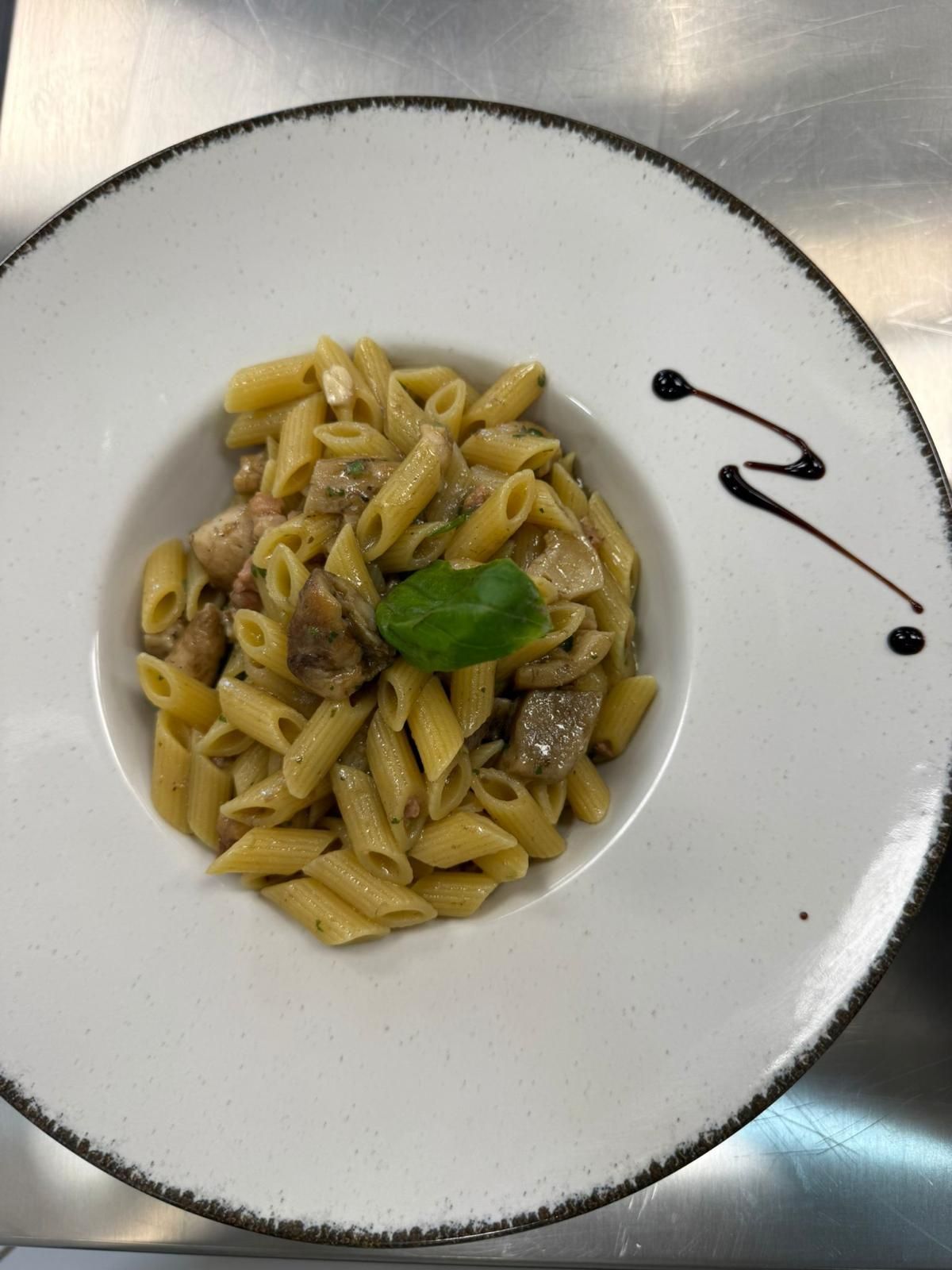 Piatto bianco con penne e guarnizione di basilico, con un filo di glassa balsamica sul bordo.