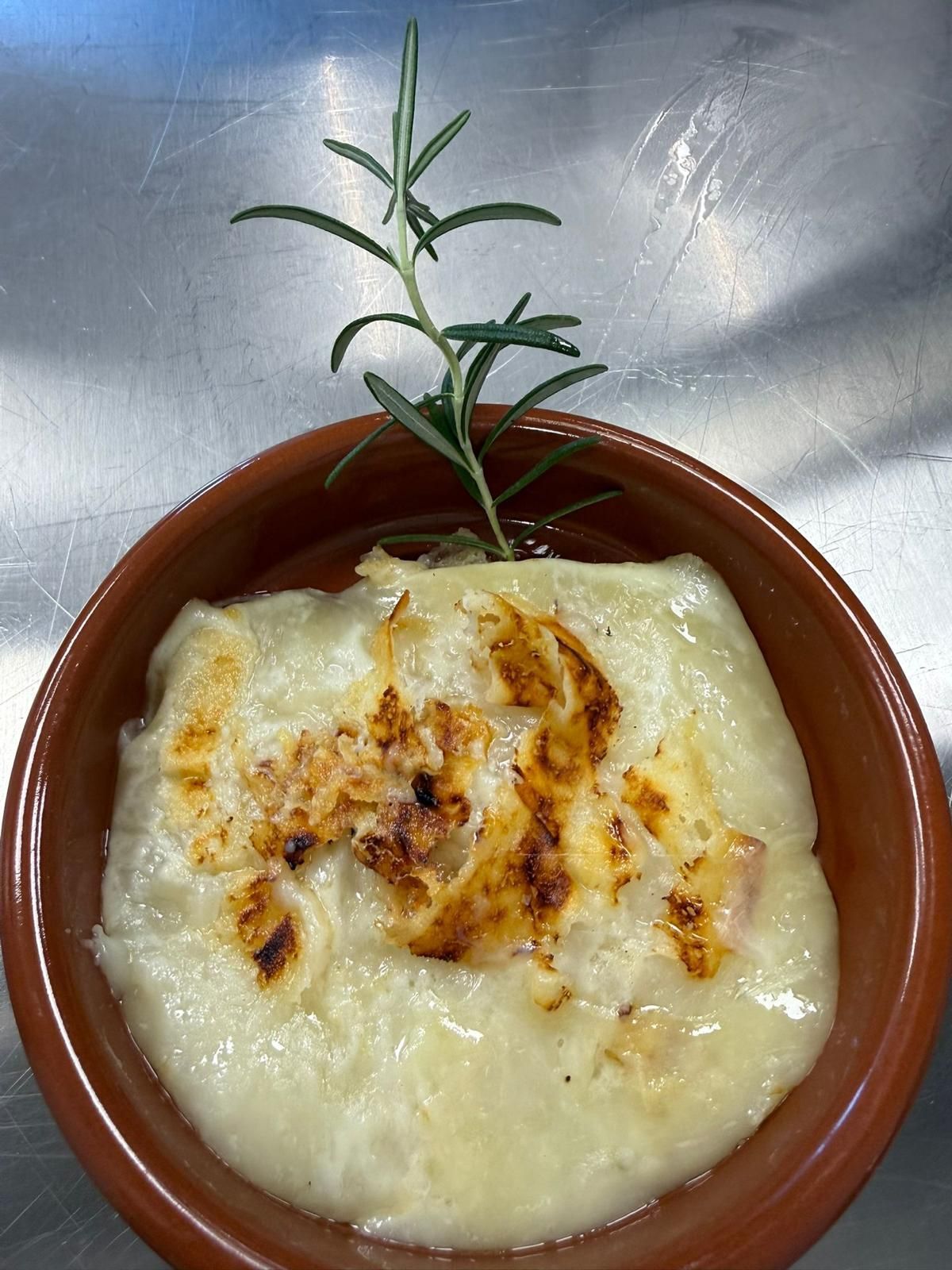 Piatto cremoso cotto al forno in una ciotola marrone, guarnito con erbe aromatiche e salsa al formaggio fuso.