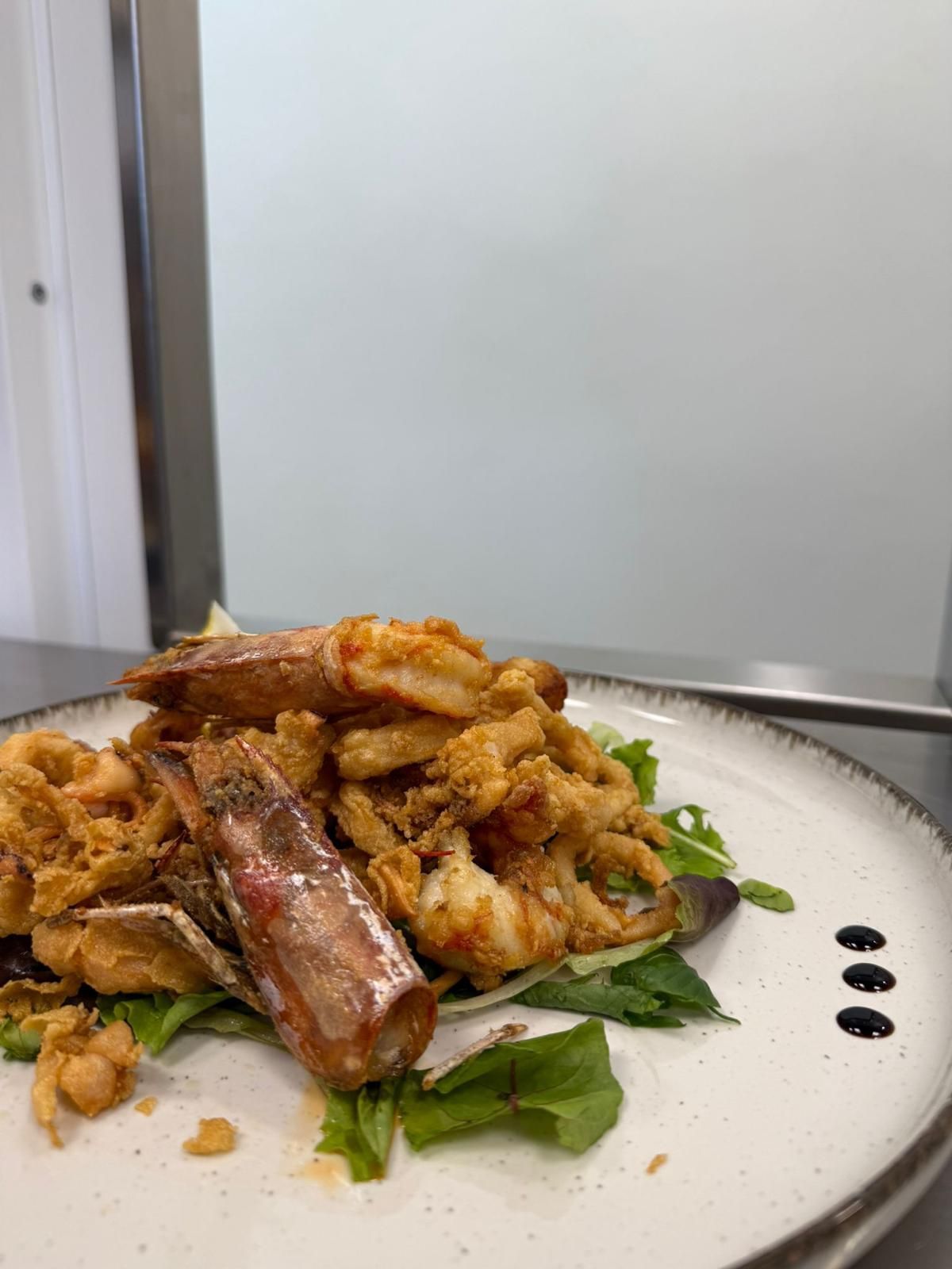 Piatto di cibo fritto con verdure e salsa su un tavolo bianco in un ambiente di cucina.