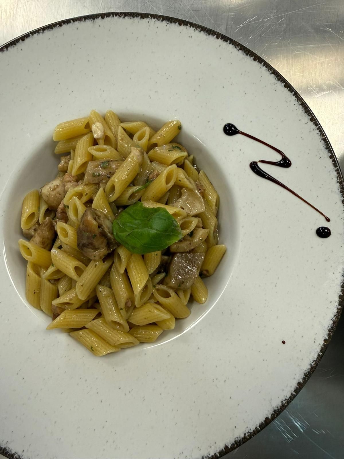 Piatto bianco con penne in salsa cremosa, guarnite con basilico e un filo di aceto balsamico a parte.