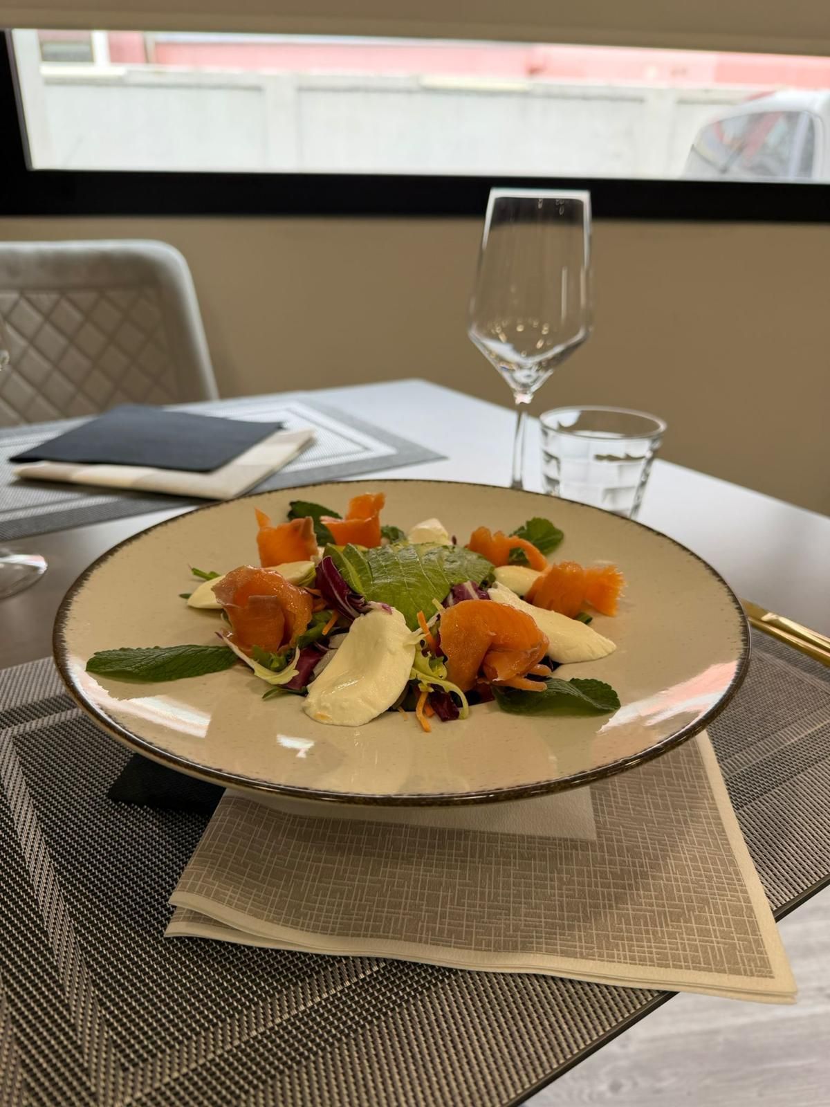 Un'insalata gourmet impiattata su un tavolo da pranzo, con un bicchiere di vino e un tovagliolo accanto.