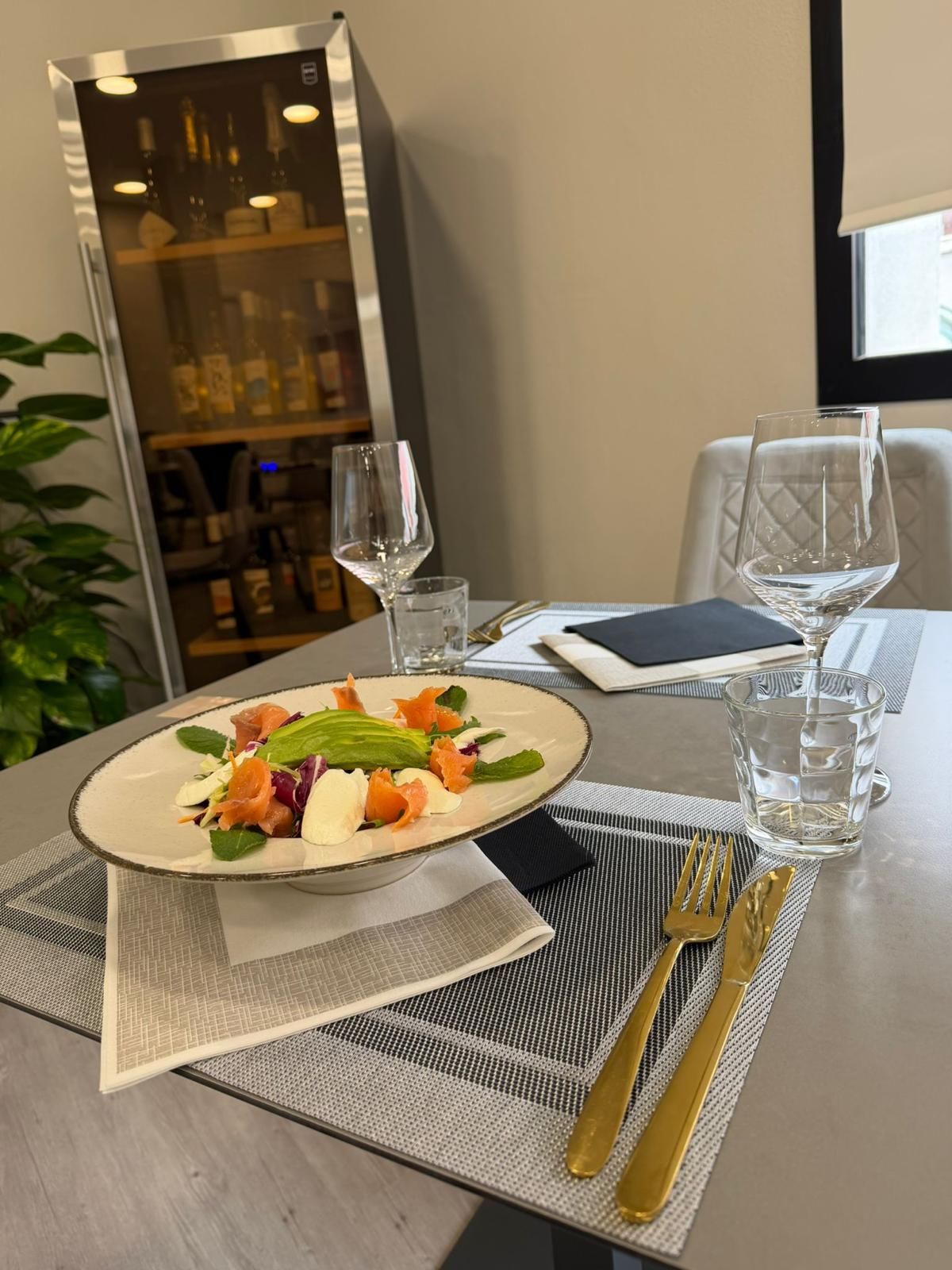 Un tavolo da pranzo apparecchiato con cura, con un piatto da insalata, bicchieri da vino, posate e una credenza sullo sfondo.