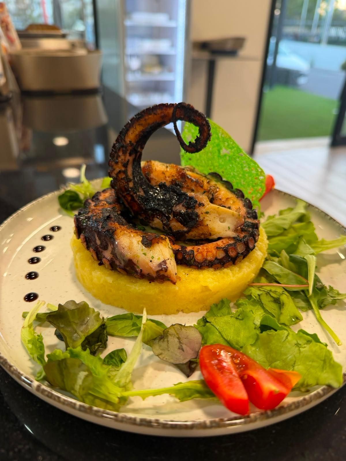 Calamari grigliati su polenta gialla con verdure e fette di pomodoro su un piatto bianco