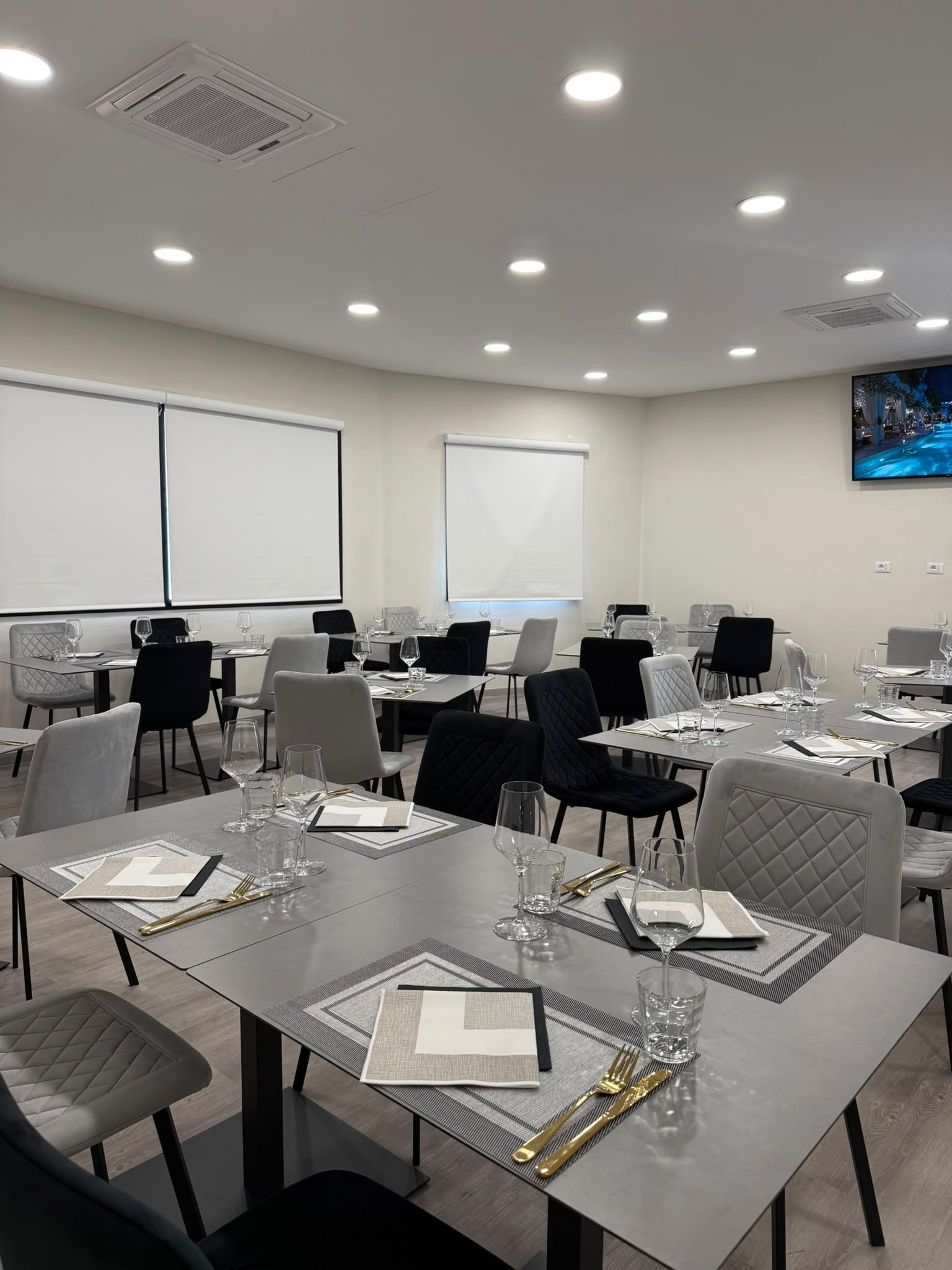 Sala da pranzo moderna e luminosa con tavoli apparecchiati con cura, sedie nere e luci a soffitto.