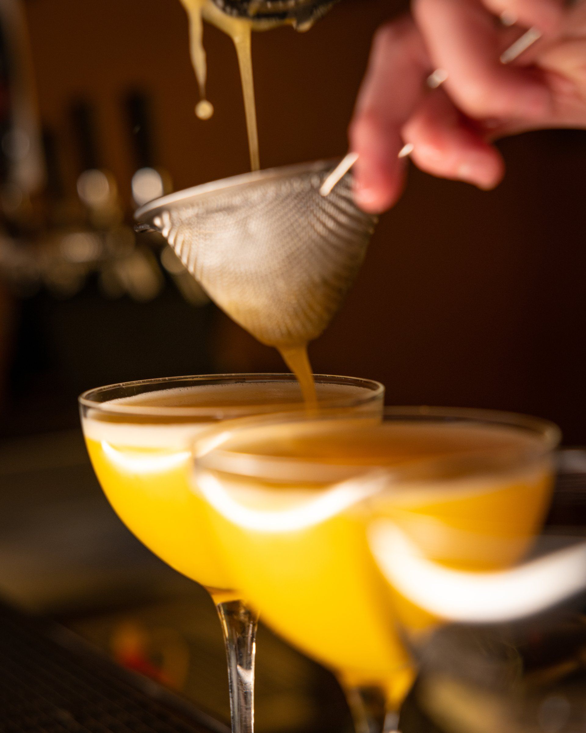 Bartender strains signature cocktail into coupe glasses.