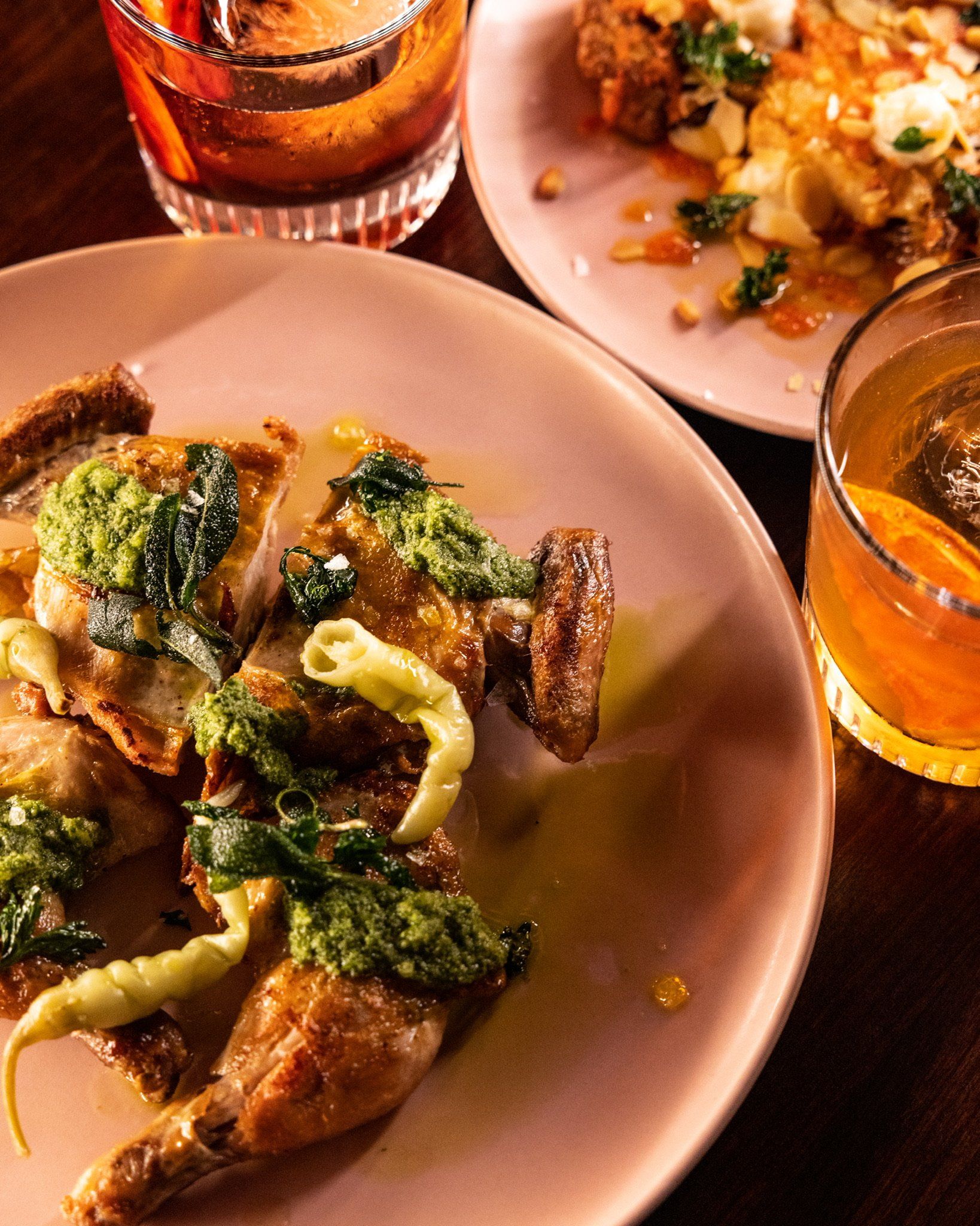 Roasted chicken and cauliflower dishes on pink plates with cocktails.
