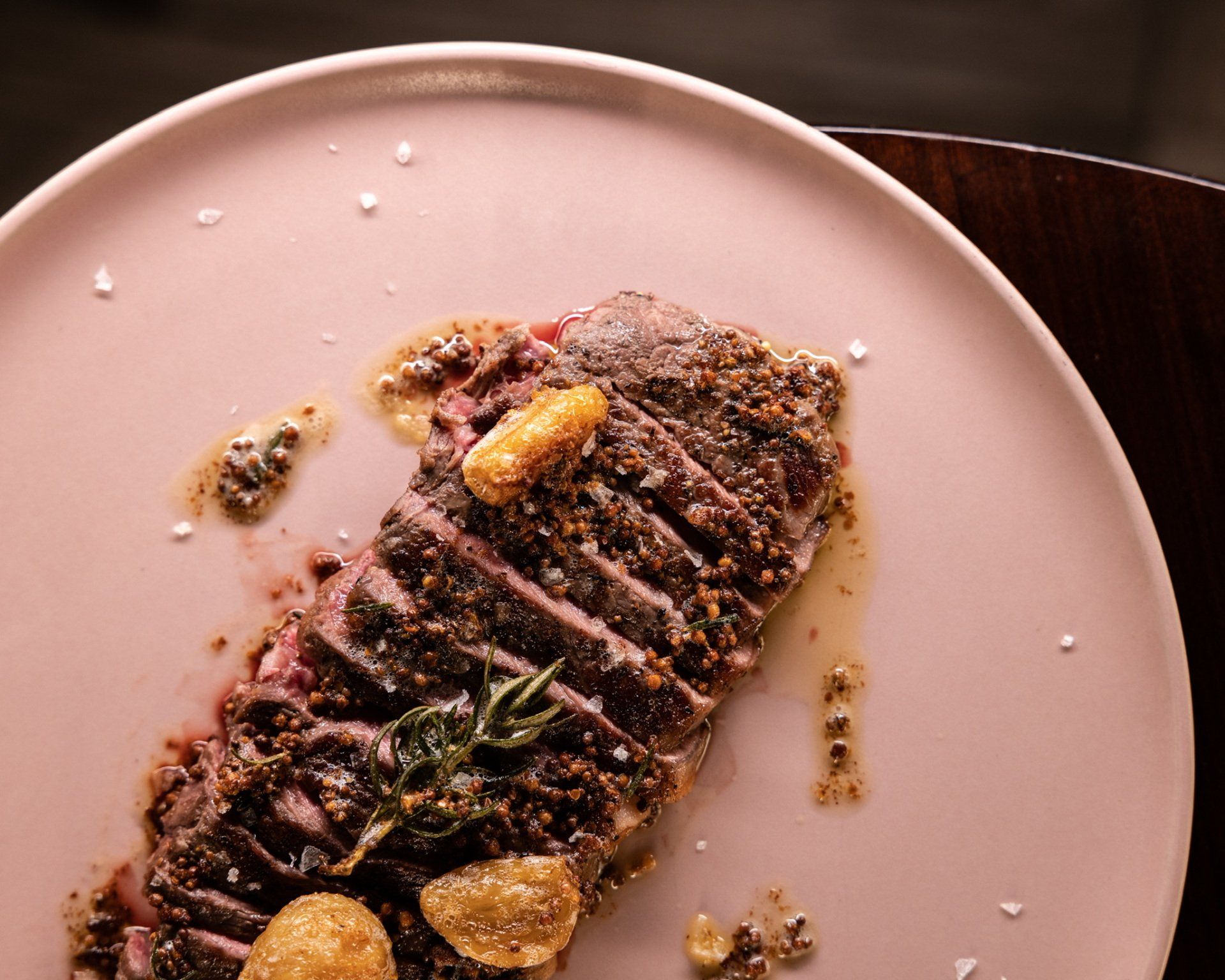 Sliced steak on a pink plate, garnished with herbs and sauce.