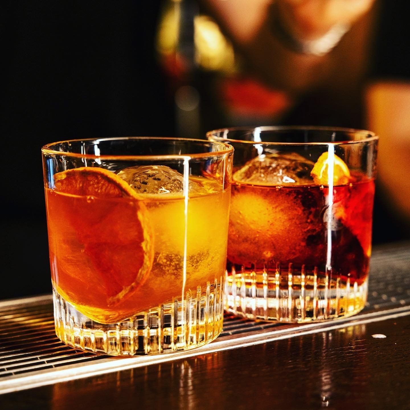 Two old fashioned cocktails in lowball glasses with ice and citrus garnishes.