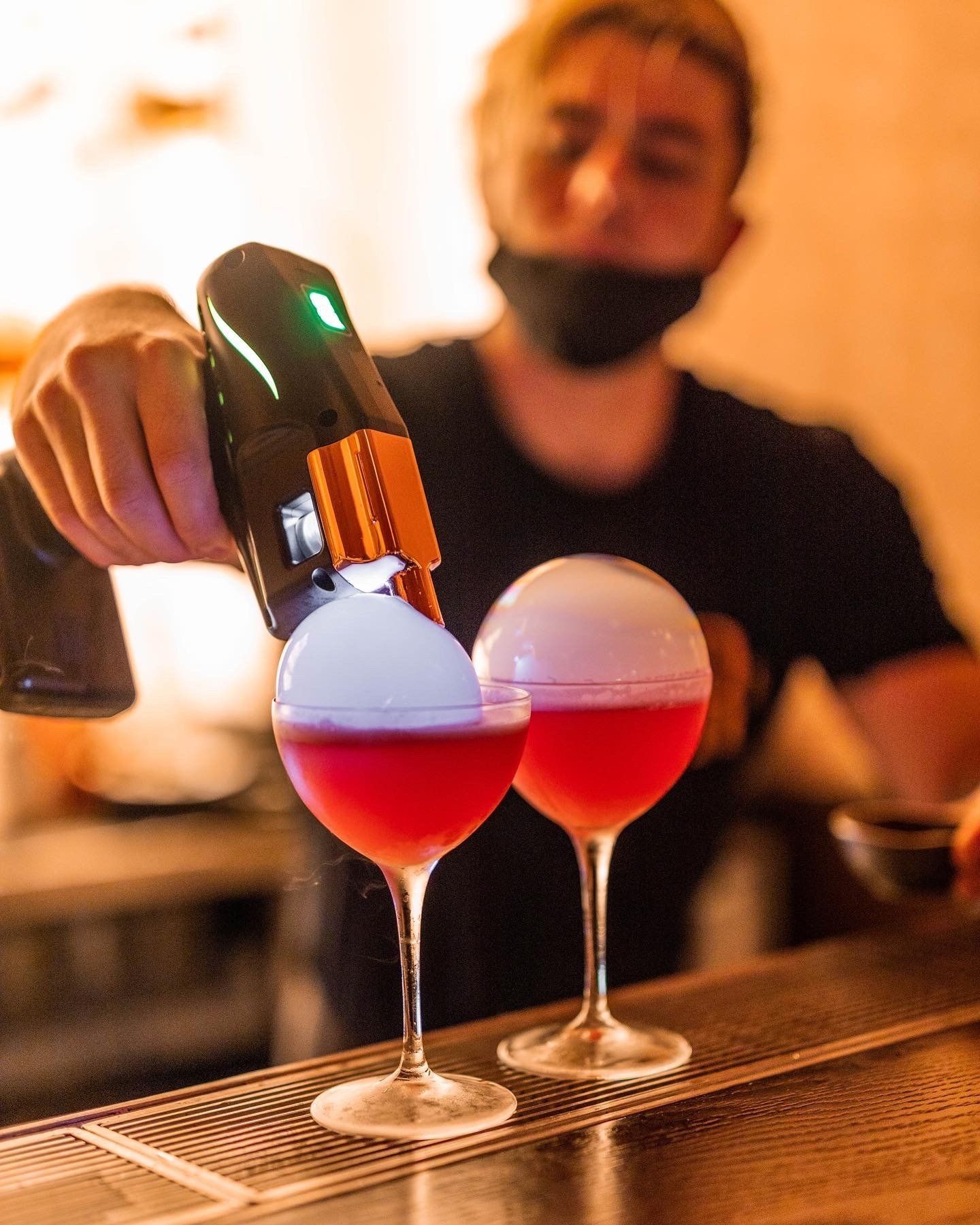 Bartender smoking two pink cocktails with a handheld smoker.