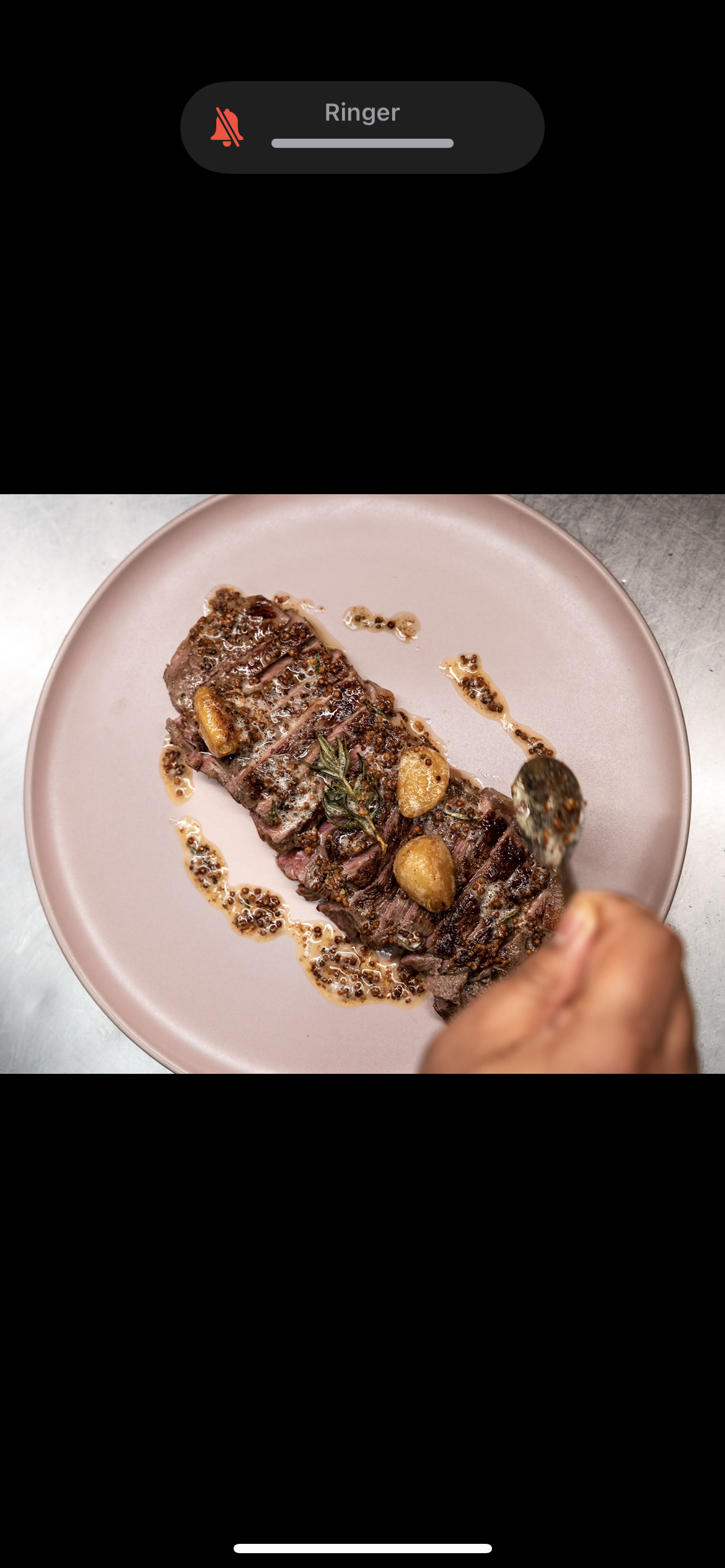 A cooked steak on a pink plate with garnish, being prepared by a hand.