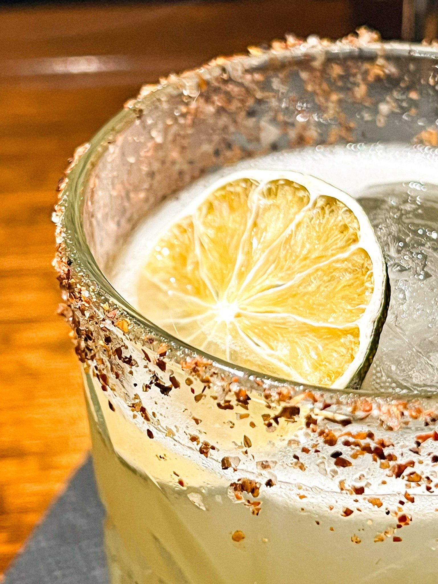 Close-up of a spicy margarita cocktail in a glass with a spiced rim, lime garnish, and ice.