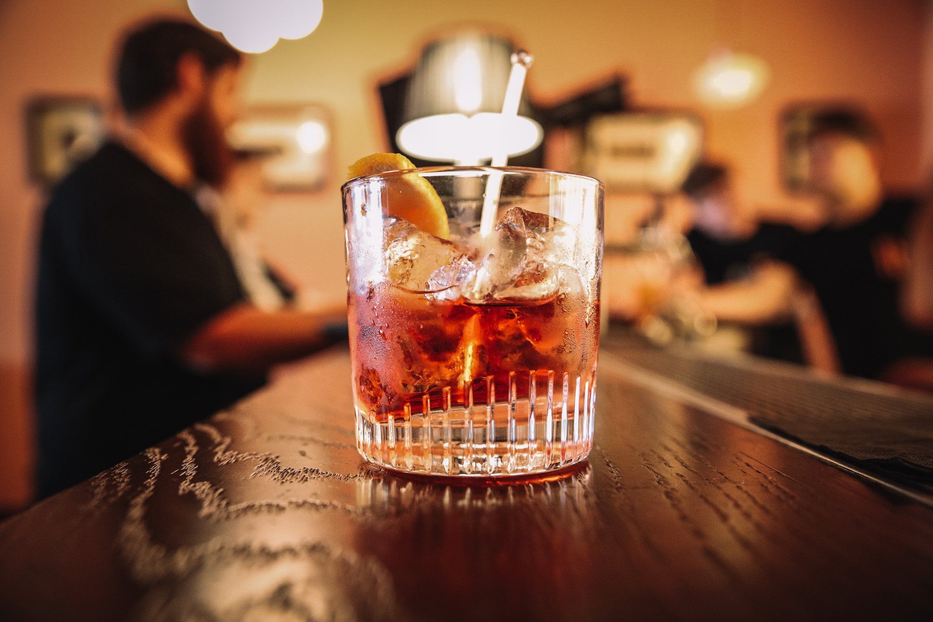 Cocktail in a glass with ice and orange slice on a bar with blurred background of a bar.