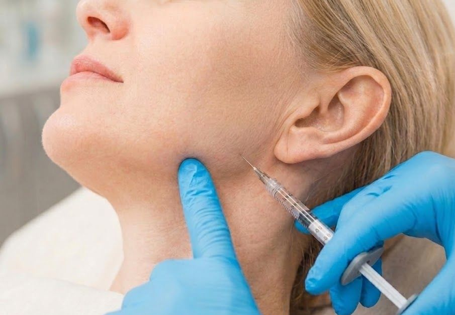 Gloved clinician injecting filler into a woman’s chin and jawline area.