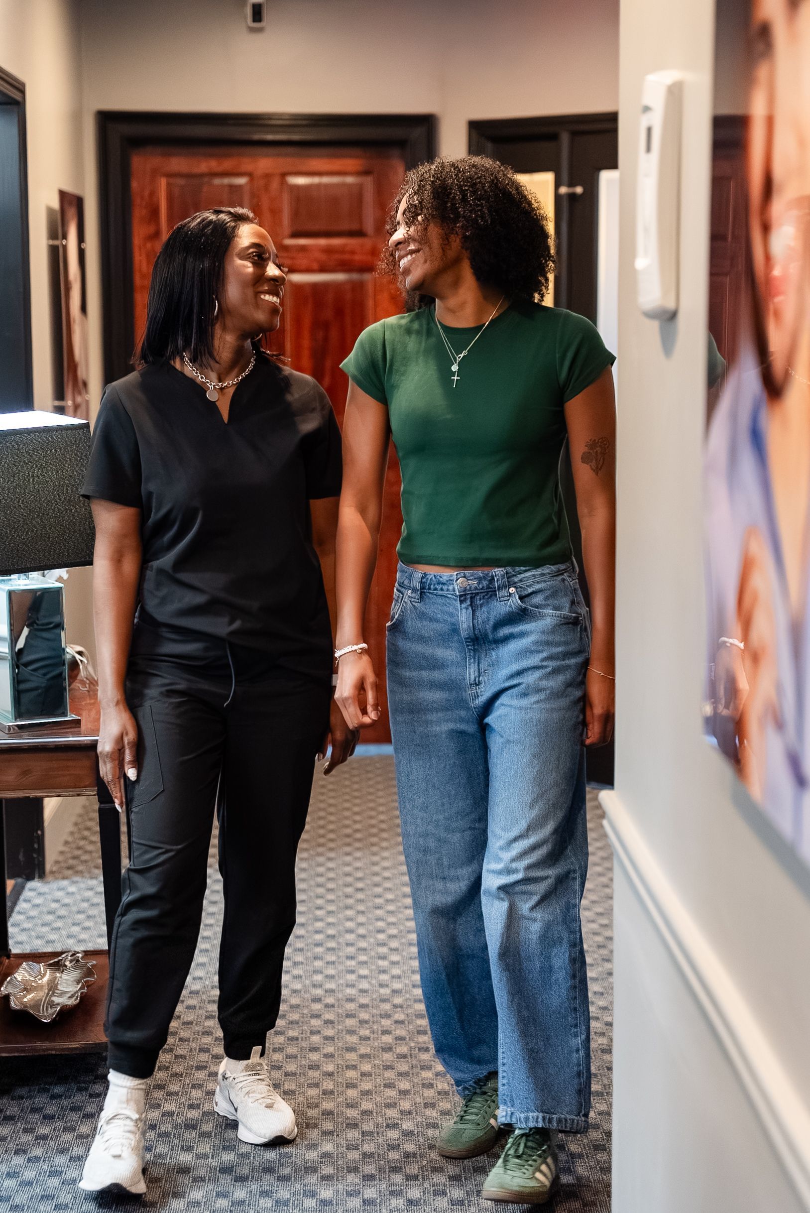 Two people walk hand in hand down a hallway, smiling, in casual clothes.