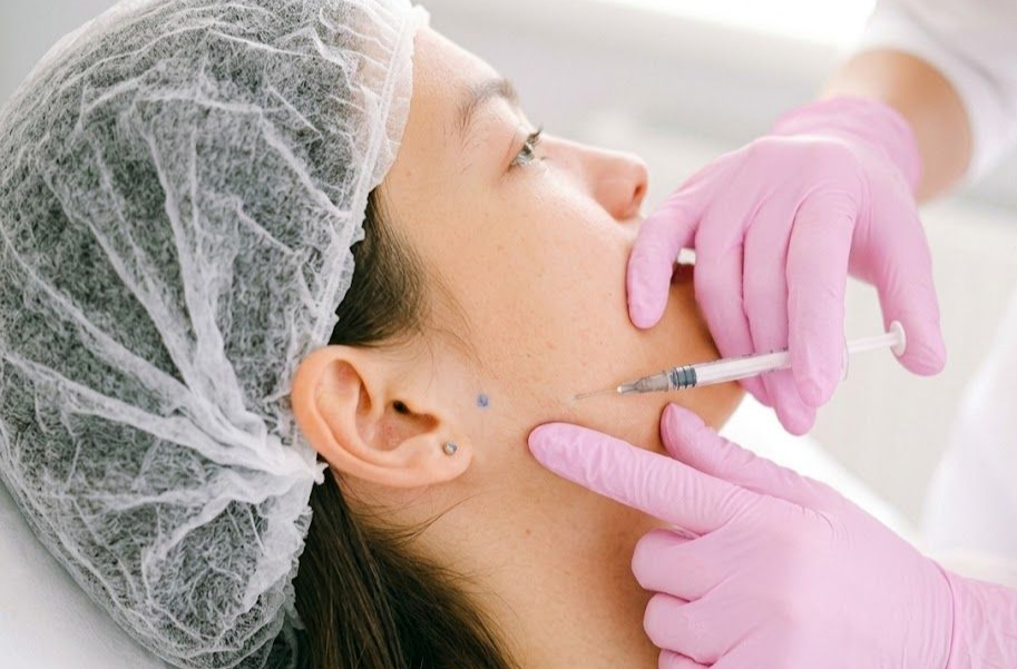 Gloved clinician giving a cheek injection to a patient in a medical setting.