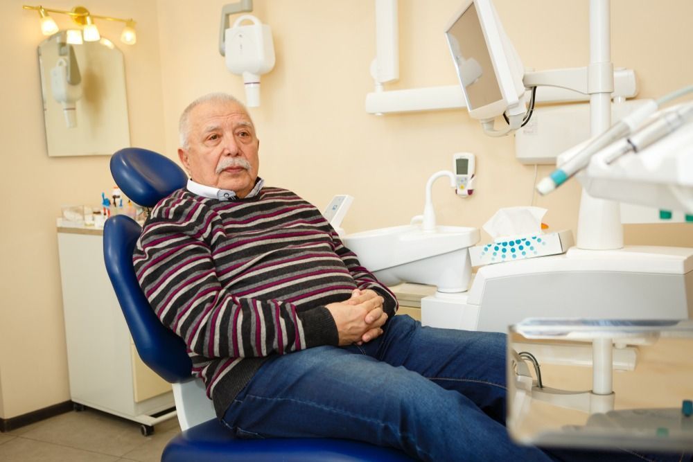 Man reclining in a dental chair during a checkup, with dental equipment and mirror nearby.