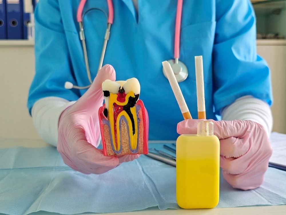 Dentist holding a tooth model and dental tools beside a yellow cup of liquid
