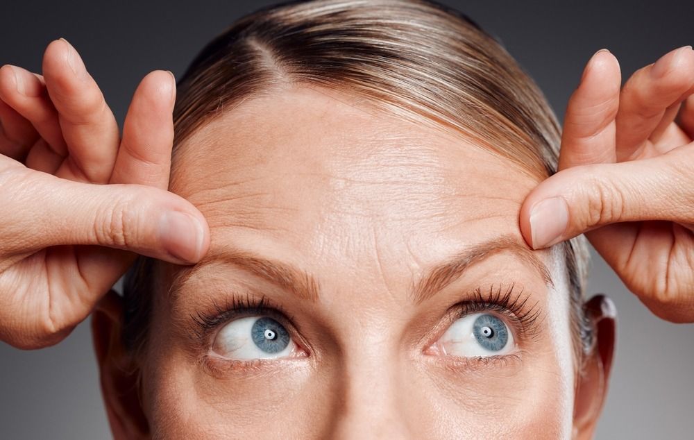 Close-up of a woman pointing at her eyebrows, with blue eyes looking upward