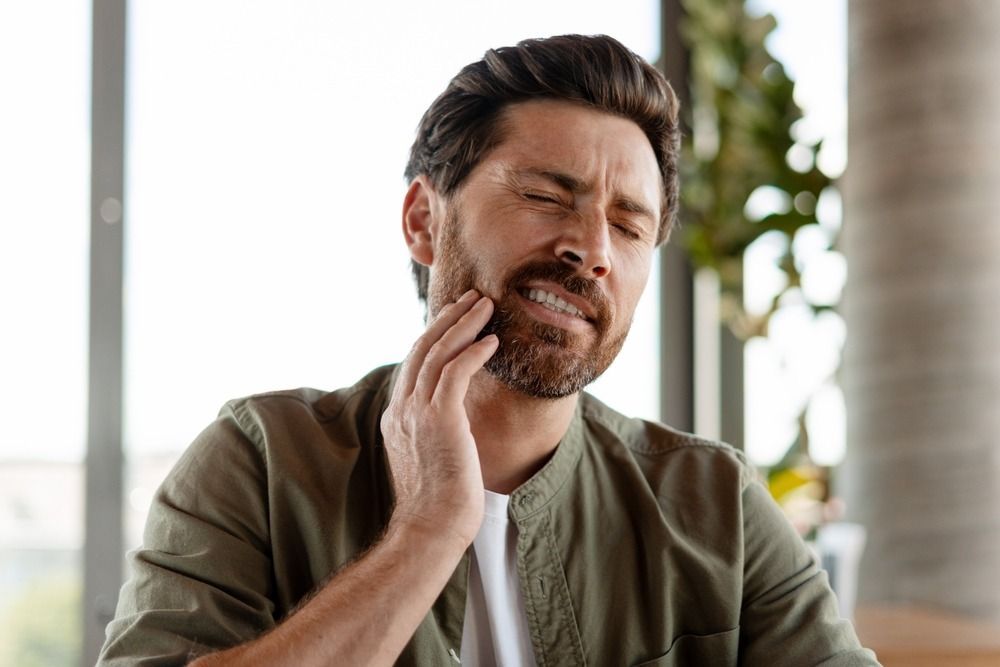 Man grimacing and holding his jaw in pain indoors