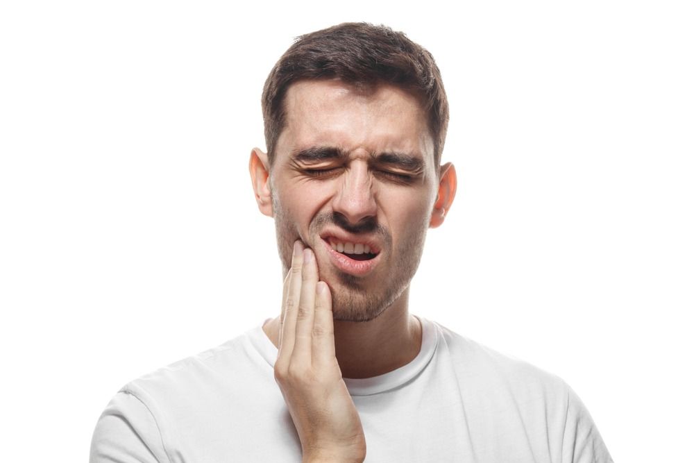 Man holding his cheek with a pained grimace against a white background