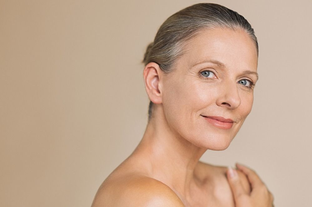 Portrait of a smiling person with hair pulled back against a beige background