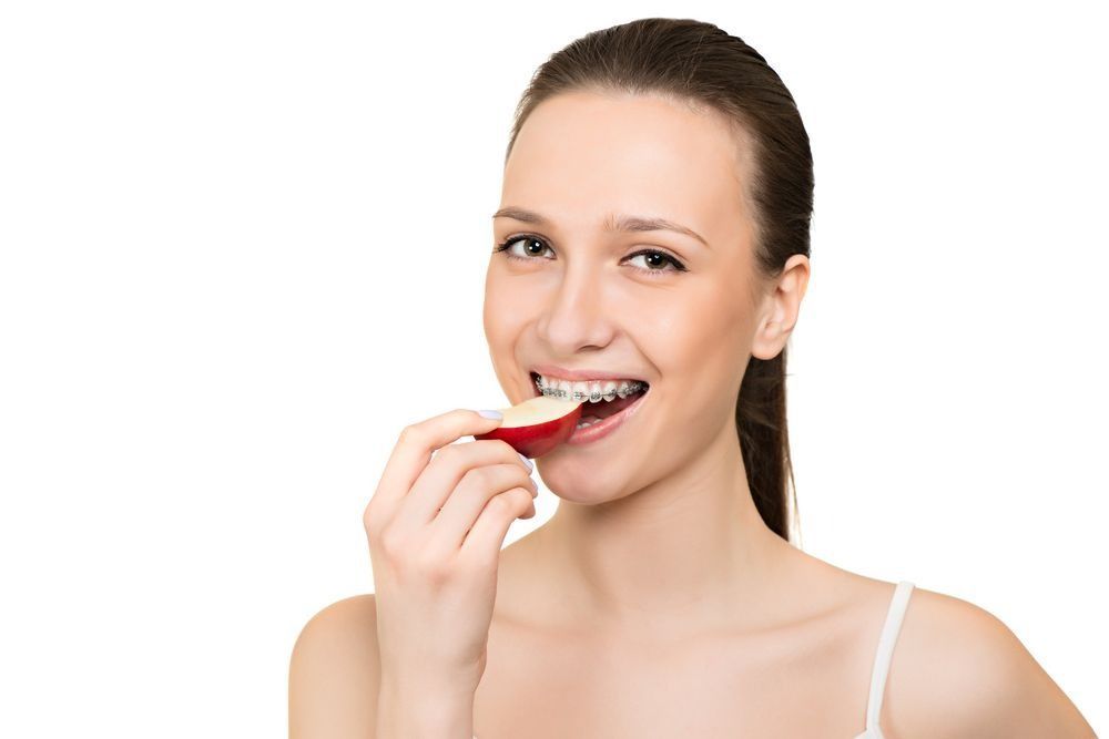 Woman brushing her teeth with a red toothbrush, smiling against a white background