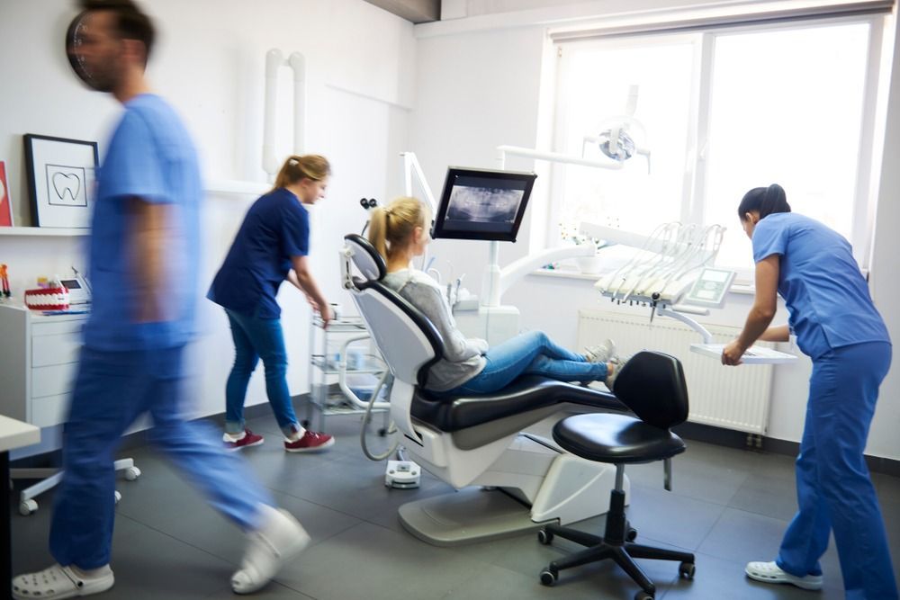 Dental clinic with patient in chair while staff in blue scrubs work around her