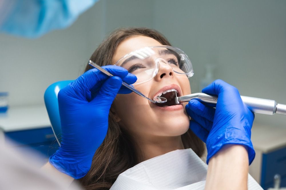 Dentist wearing blue gloves examines a patient’s teeth with dental tools and a mirror