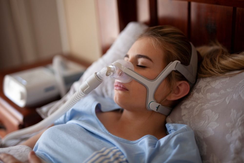 Person sleeping with a CPAP mask in a bed, wearing a light blue shirt.