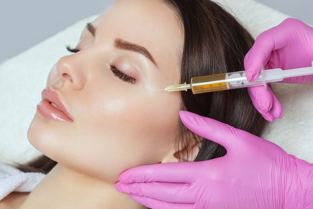 Cosmetic injection near a woman's cheek by gloved hands holding a syringe