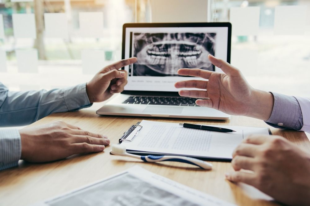 Hands pointing at dental X-rays on a laptop during a meeting at a desk