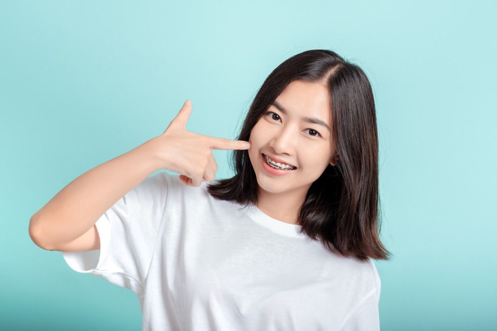 Smiling woman in a white shirt pointing to her face against a turquoise background