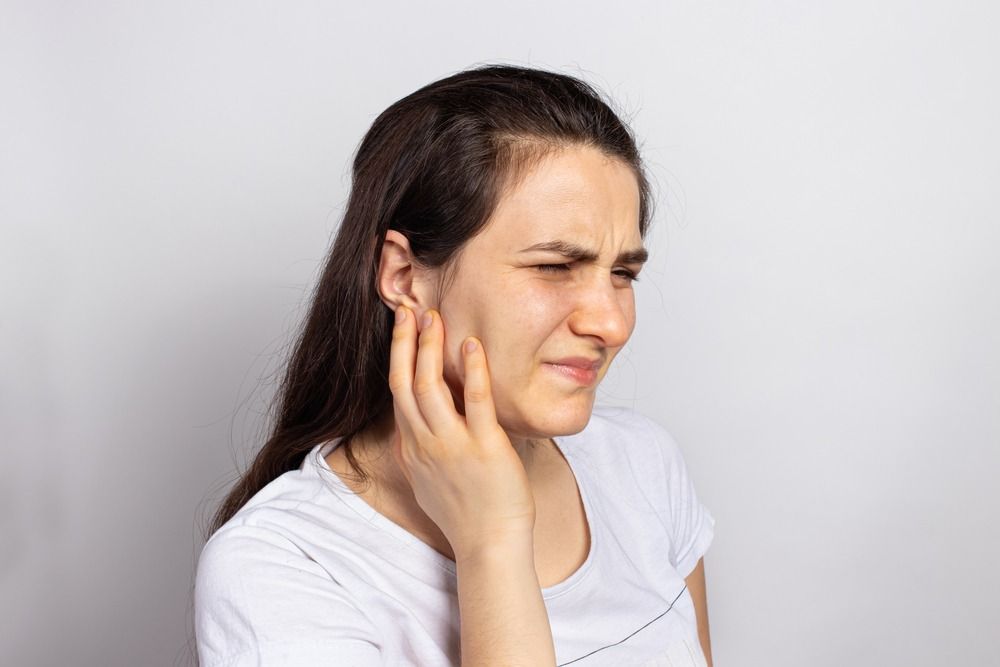Woman holding her cheek with a pained expression, suggesting tooth or ear pain